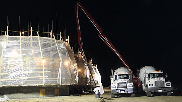 Skilled construction workers use cranes and trucks for building projects under nighttime lighting.