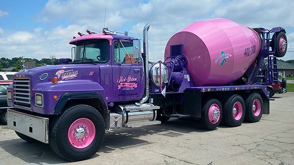 Cement mixer truck painted in pink and purple with company branding in an outdoor lot.