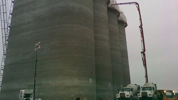 Large concrete silos with cement trucks at an industrial site.