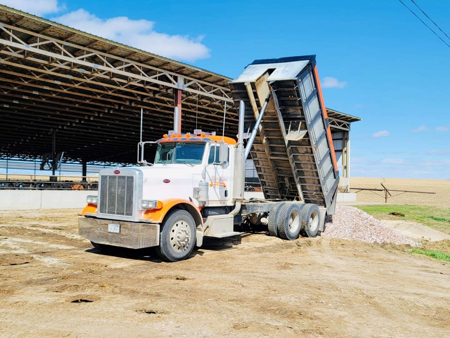 Earthmoving dump truck unloading gravel at construction or farming site.