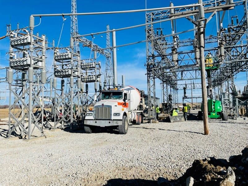 High-voltage power substation with electrical infrastructure and construction workers.